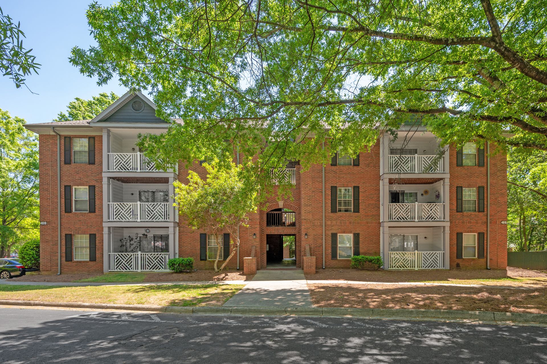 Sharon Oaks red-brick apartment homes and white balconies beneath a canopy of mature green trees